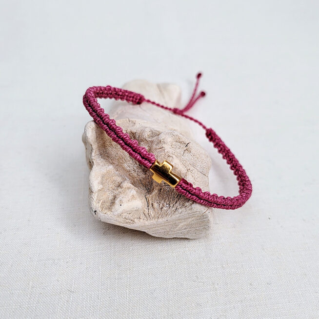 pulsera cruz malva hecha a mano con poliéster encerado y pieza central con baño de oro, con cierre ajustable mediante un nudo corredero